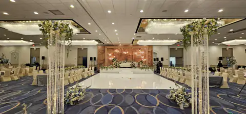 Closer view of crystal-strand pillars topped with white and blue florals, framing a white dance floor that leads to a champagne drape stage.